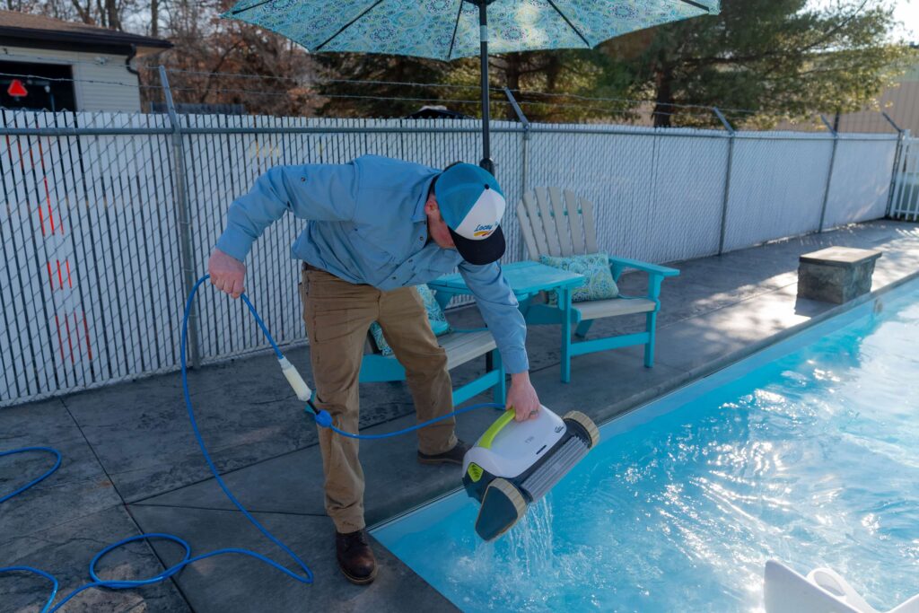 A man cleans a pool using an automated pool cleaner.