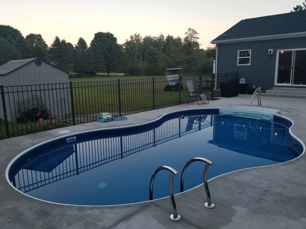 A freeform in-ground pool behind a home in a fenced-off patio area.